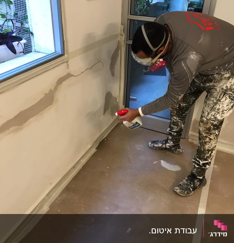 אדם מרסס חומר איטום על קיר עם סדקים